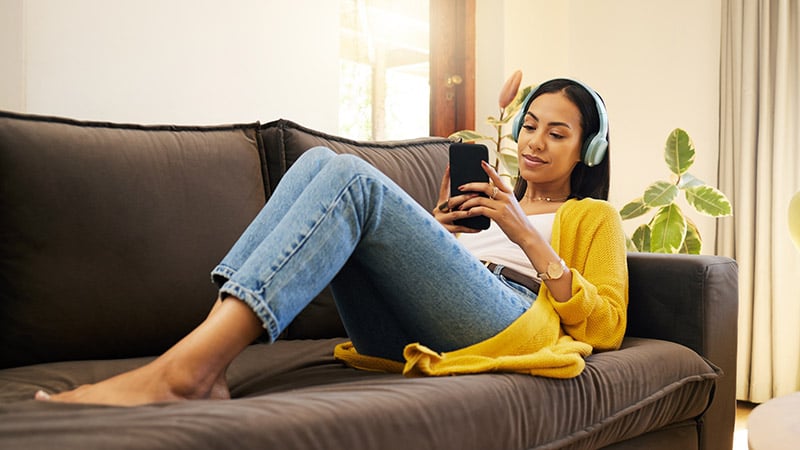 Young female relaxing on a couch listening to music with headphones on mobile smartphone