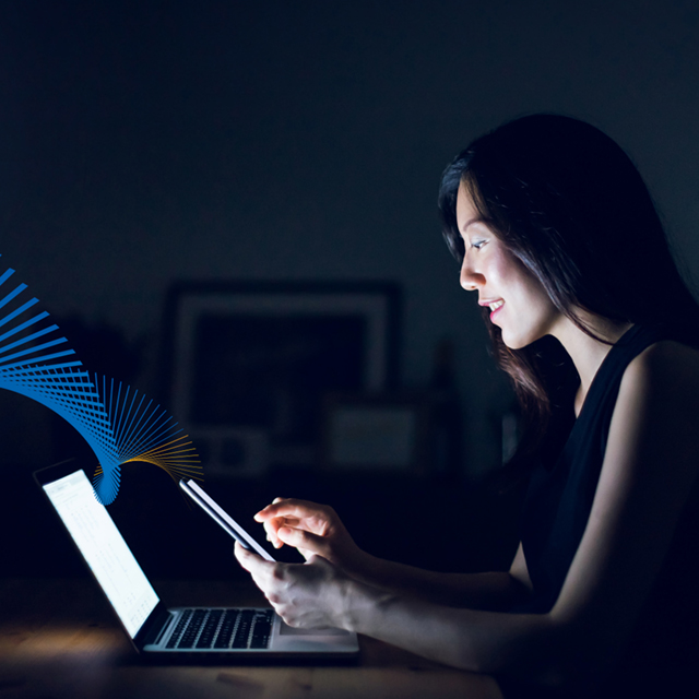 Women sitting in front of laptop, but looking at mobile phone.