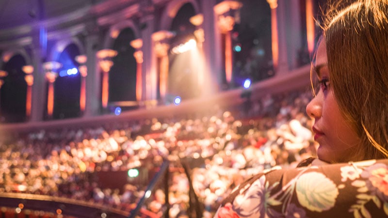 An asian woman watching a west end show with blurred crowds of seated people in background