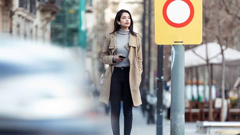 Pretty young woman crossing the street while listen to music with the wireless earphones.